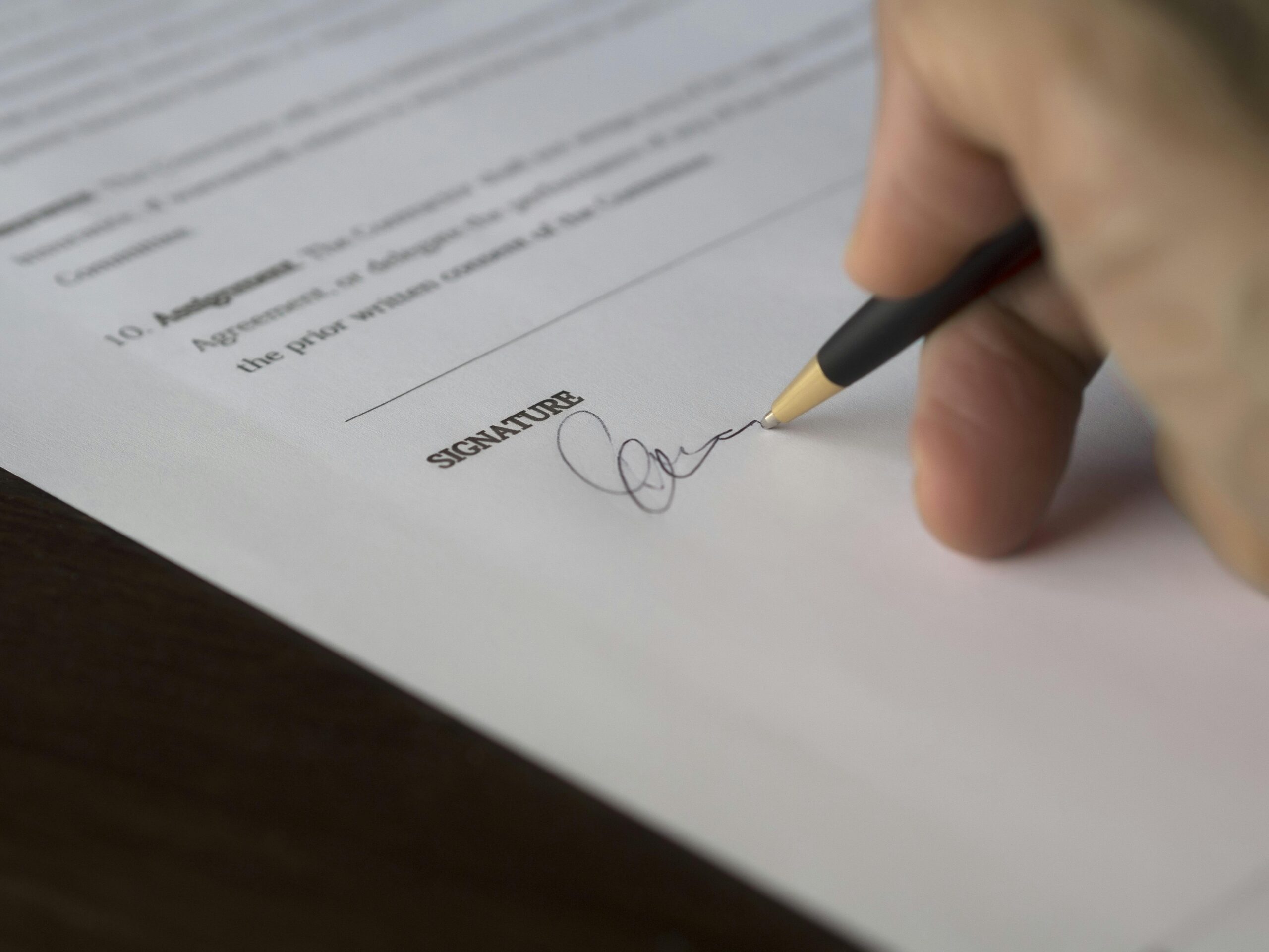 An individual signing a formal, legal document using an ink pen with a gold tip and black stalk